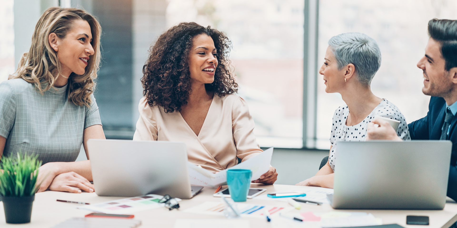 equipe formada por uma negra, uma branca uma mulher mais velha e homem na mesa de trabalho